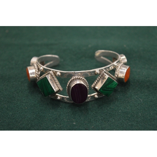 1099 - A heavy silver bangle set with coloured stones.