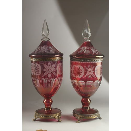 49 - A LARGE PAIR OF BOHEMIAN RUBY TINTED URNS AND COVERS on metal bases with claw feet. 54cms high, one ... 