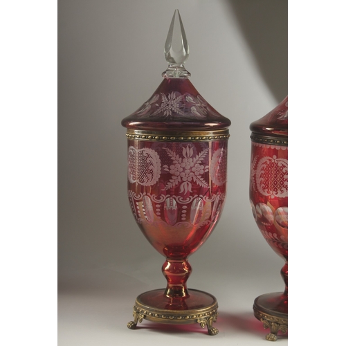 49 - A LARGE PAIR OF BOHEMIAN RUBY TINTED URNS AND COVERS on metal bases with claw feet. 54cms high, one ... 