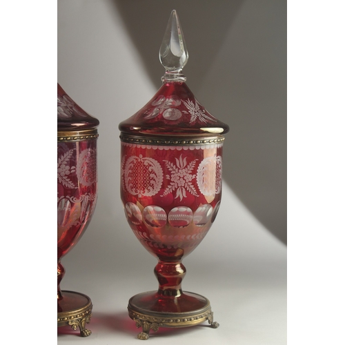 49 - A LARGE PAIR OF BOHEMIAN RUBY TINTED URNS AND COVERS on metal bases with claw feet. 54cms high, one ... 