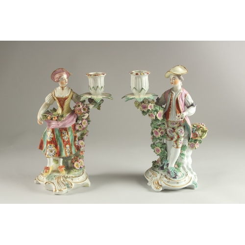 61 - A PAIR OF DERBY FIGURE CANDLESTICKS, as a woman and man, encrusted with flowers, each with a candle ... 