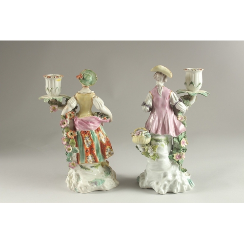 61 - A PAIR OF DERBY FIGURE CANDLESTICKS, as a woman and man, encrusted with flowers, each with a candle ... 