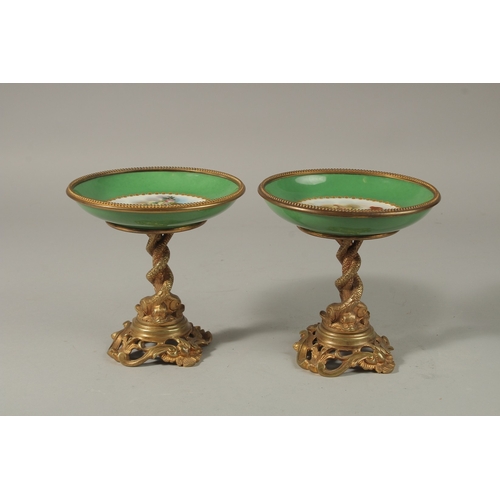 71 - A GOOD PAIR OF SEVRES APPLE GREEN PORCELAIN CIRCULAR TAZZAS painted with cupids, the ormolu bases wi... 