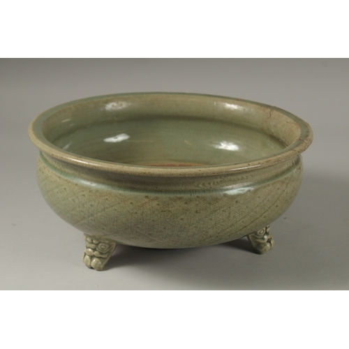 1043 - A 16TH CENTURY GREEN GLAZED DEEP CIRCULAR BOWL, raised on three lion feet. 15cm high, 32cm wide.