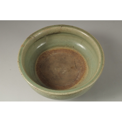 1043 - A 16TH CENTURY GREEN GLAZED DEEP CIRCULAR BOWL, raised on three lion feet. 15cm high, 32cm wide.