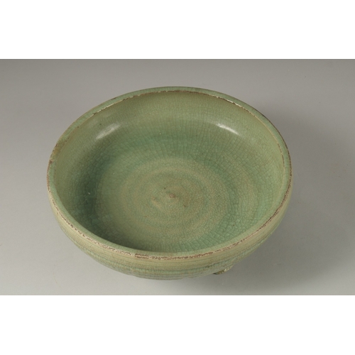 1044 - A 16TH CENTURY GREEN GLAZED DEEP CIRCULAR BOWL, raised on three lion feet. 13cm high, 30cm wide.