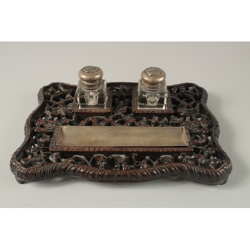 1266 - A CHINESE CARVED OPENWORKED HARDWOOD DESK STAND with two glass inkwells and brush rest, 31cm x 23cm.