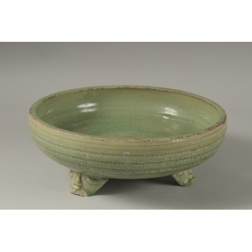 173 - A 16TH CENTURY GREEN GLAZED DEEP CIRCULAR BOWL, raised on three lion feet. 13cm high, 30cm wide.