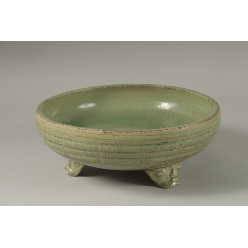 173 - A 16TH CENTURY GREEN GLAZED DEEP CIRCULAR BOWL, raised on three lion feet. 13cm high, 30cm wide.