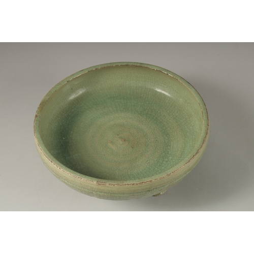 173 - A 16TH CENTURY GREEN GLAZED DEEP CIRCULAR BOWL, raised on three lion feet. 13cm high, 30cm wide.