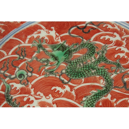 303 - A CHINESE CORAL RED GROUND PORCELAIN DISH, with painted enamels depicting green dragons on stylised ... 