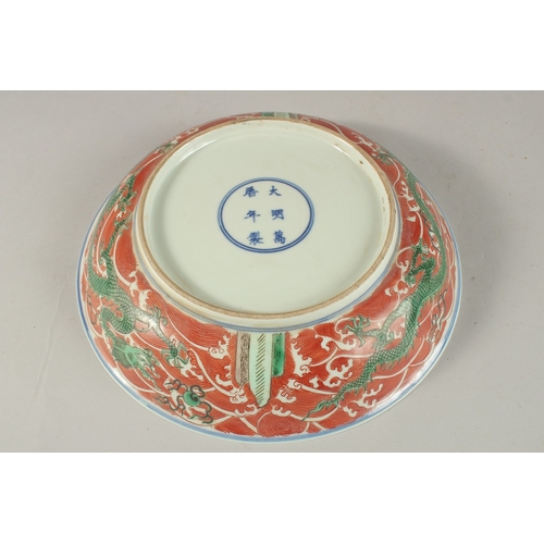 303 - A CHINESE CORAL RED GROUND PORCELAIN DISH, with painted enamels depicting green dragons on stylised ... 