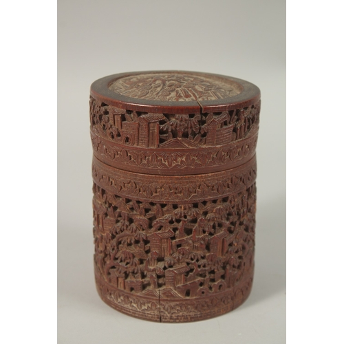 61 - A CHINESE FINELY CARVED BAMBOO LIDDED BRUSH POT, with a continuous village scene, 15cm high.