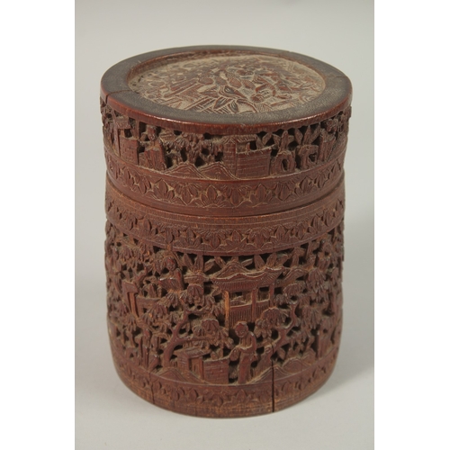 61 - A CHINESE FINELY CARVED BAMBOO LIDDED BRUSH POT, with a continuous village scene, 15cm high.