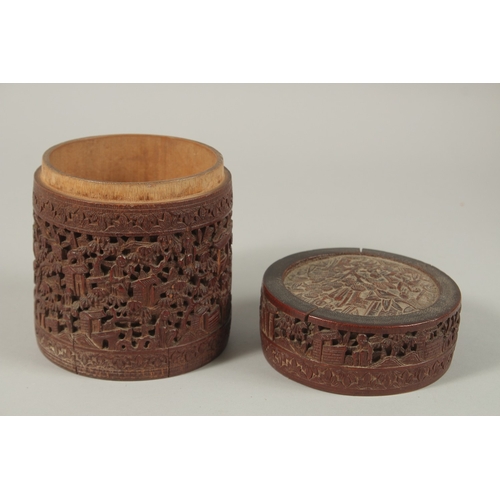 61 - A CHINESE FINELY CARVED BAMBOO LIDDED BRUSH POT, with a continuous village scene, 15cm high.