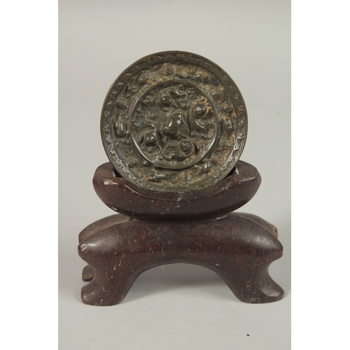 67 - A CHINESE CIRCULAR BRONZE MIRROR, with carved soapstone stand, mirror 9cm diameter.