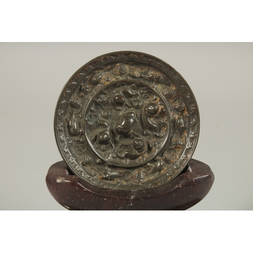 67 - A CHINESE CIRCULAR BRONZE MIRROR, with carved soapstone stand, mirror 9cm diameter.