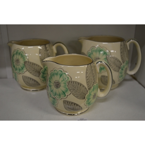 591 - A graduated set of three Grays Pottery jugs decorated with flowers and leaves in green, grey and sil... 