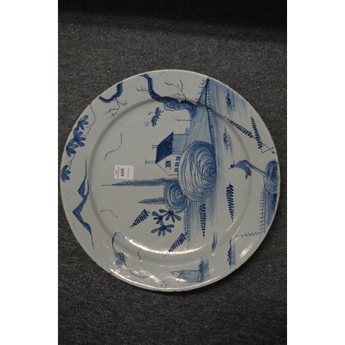 608 - An 18th century tin glazed blue and white charger decorated with a house, trees and a boat.