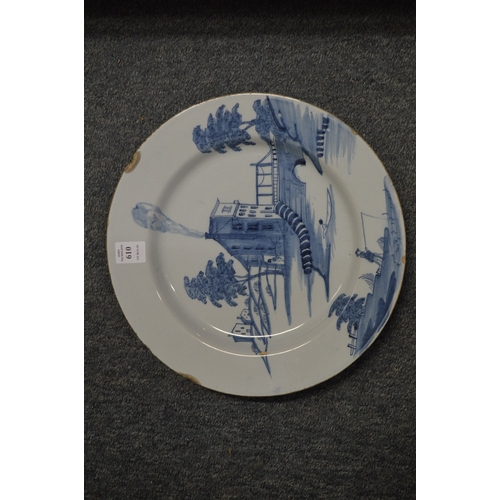 610 - An 18th century tin glazed blue and white charger decorated with building by a bridge with a man fis... 