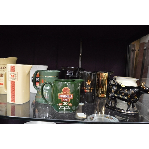 78 - A large quantity of pub jugs advertising Bells and other whiskies etc together with a cow creamer an... 