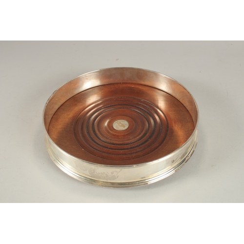 1148 - A LARGE SILVER CIRCULAR WINE COASTER with wooden base. 8ins diameter.