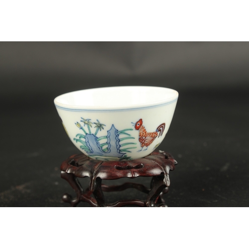 620 - A CHINESE WUCAI CHICKEN TEA CUP on a wooden stand. Cup: 8cms diameter.