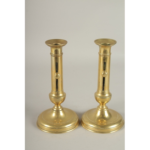 695 - A PAIR OF CIRCULAR BRASS CANDLESTICKS WITH PUSHERS. 21cms high.