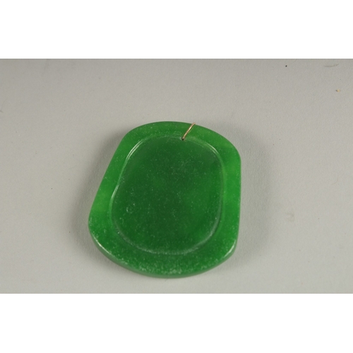 921 - A CARVED APPLE GREEN JADE PENDANT with gold ring.