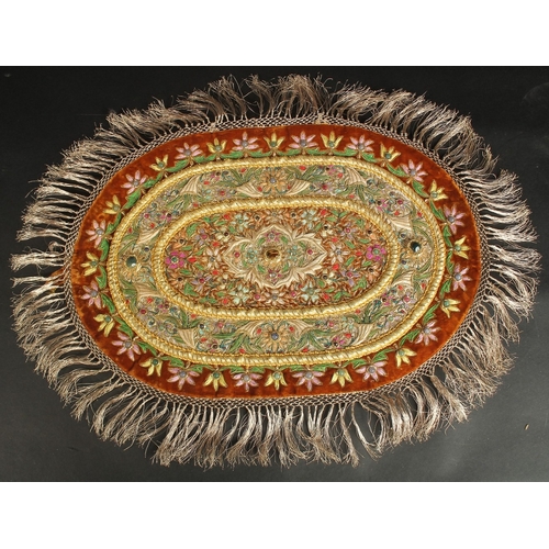 283 - AN INDIAN EMBROIDERED OVAL TEXTILE WITH VARIOUS INSET STONES.