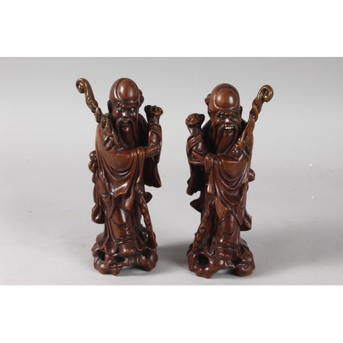 26 - A PAIR OF 19TH CENTURY CHINESE CARVED HARDWOOD FIGURES, with inset eyes and teeth, 21cm high.