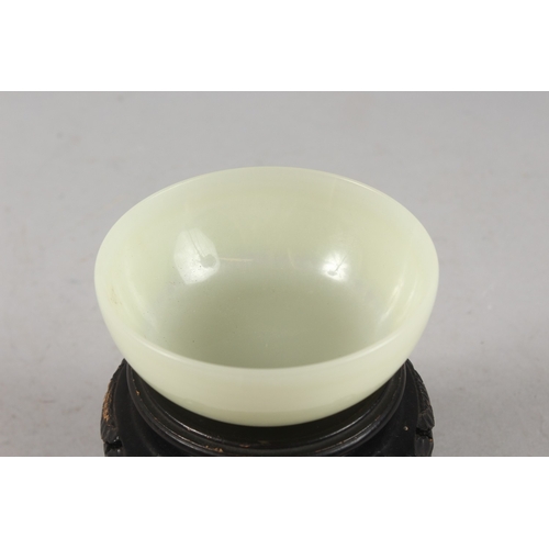 275 - A CHINESE JADE BOWL ON HARDWOOD STAND, bowl 10cm diameter.