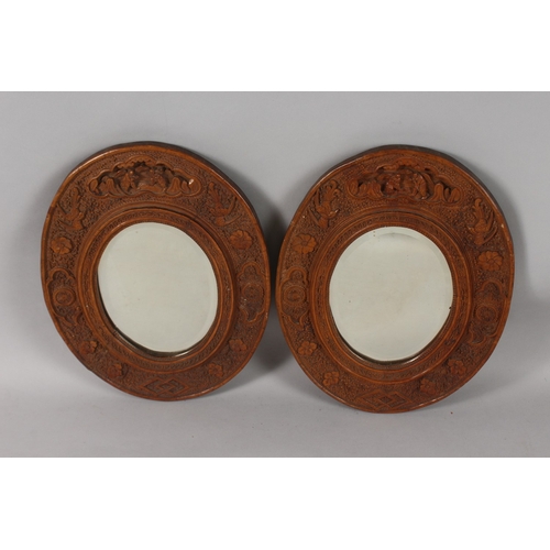 399 - A PAIR OF CHINESE CARVED SANDALWOOD OVAL MIRRORS, the frames ornately carved with foliate border inc... 