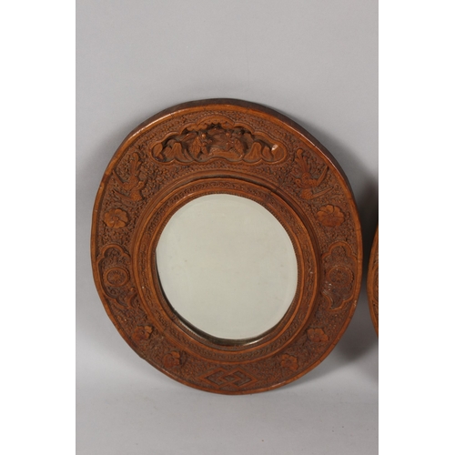 399 - A PAIR OF CHINESE CARVED SANDALWOOD OVAL MIRRORS, the frames ornately carved with foliate border inc... 