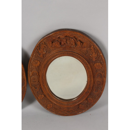 399 - A PAIR OF CHINESE CARVED SANDALWOOD OVAL MIRRORS, the frames ornately carved with foliate border inc... 