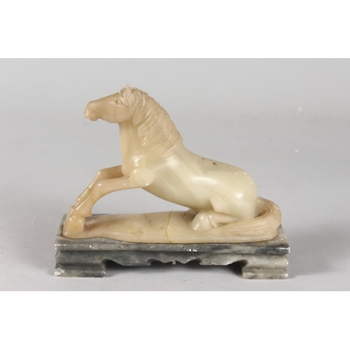 41 - A CHINESE QING DYNASTY GREEN SOAPSTONE CARVING OF A RECUMBENT HORSE, mounted to a rectangular hardst... 