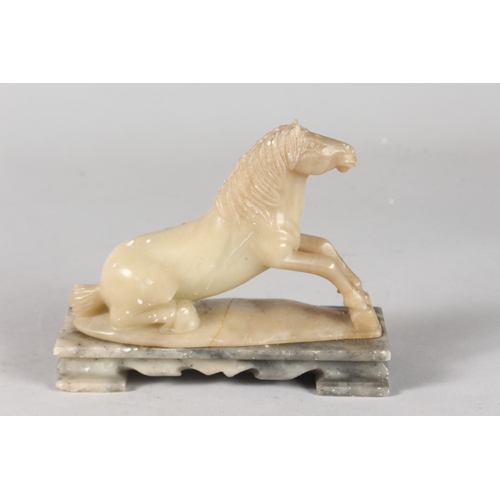 41 - A CHINESE QING DYNASTY GREEN SOAPSTONE CARVING OF A RECUMBENT HORSE, mounted to a rectangular hardst... 