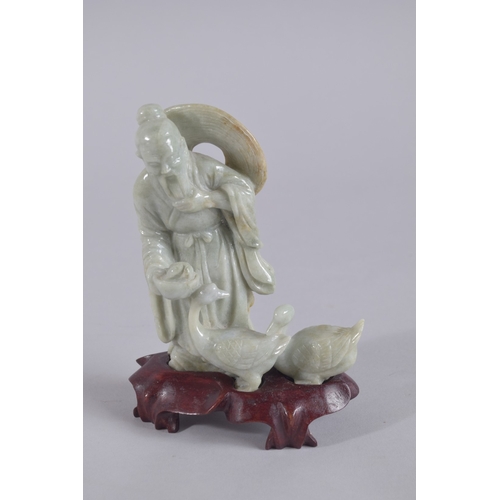 43 - A CHINESE CARVED JADEITE FIGURE ON HARDWOOD STAND, figure 13.5cm high.