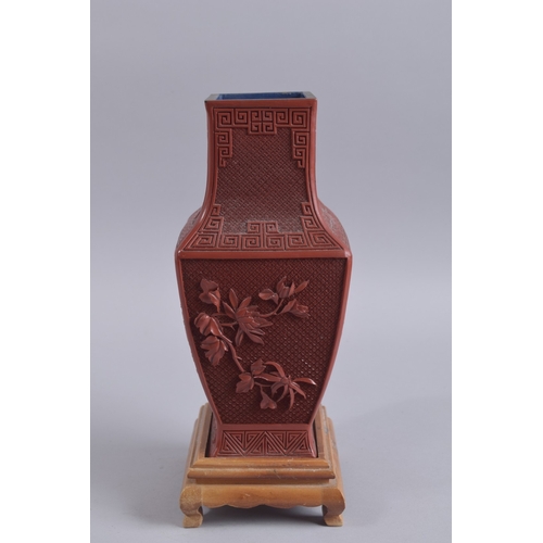 125 - A CHINESE RED CINNABAR LACQUER VASE ON WOODEN STAND, with landscape scenes and flora, 28cm high.