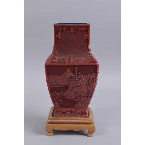 125 - A CHINESE RED CINNABAR LACQUER VASE ON WOODEN STAND, with landscape scenes and flora, 28cm high.