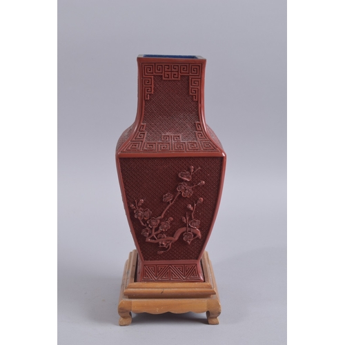 125 - A CHINESE RED CINNABAR LACQUER VASE ON WOODEN STAND, with landscape scenes and flora, 28cm high.