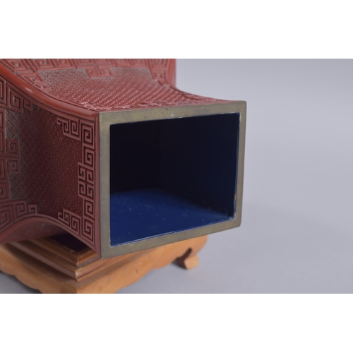 125 - A CHINESE RED CINNABAR LACQUER VASE ON WOODEN STAND, with landscape scenes and flora, 28cm high.