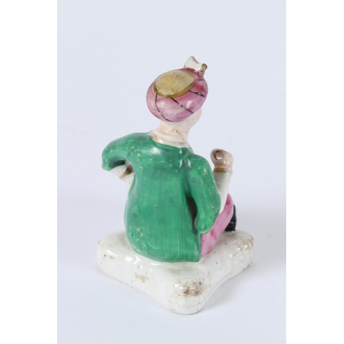 137 - A FIGURE OF A SEATED PORCELAIN TURKISH MAN SITTING GROSS-LEGGED ON A CUSHION. 10cms high.