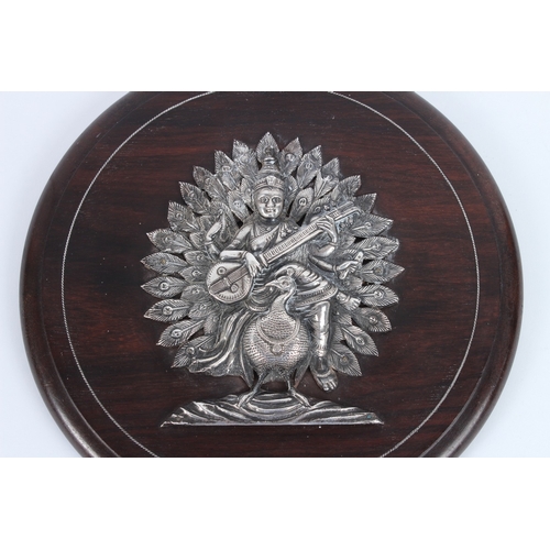 227 - A FINE INDIAN SILVER HINDU DEITY on a wooden plaque. 23cms diameter.