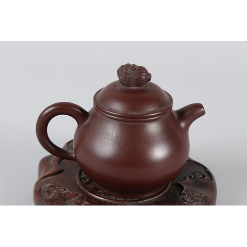 4 - A FINE CHINESE YIXING TEAPOT with hardwood stand.  12cms high.