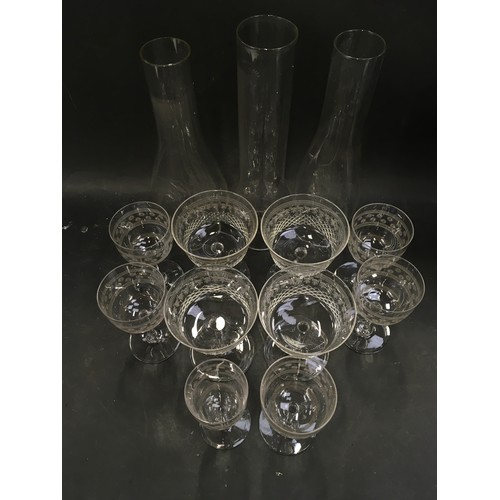 111 - Three vintage glass oil lamp chimneys together with a collection of etched stemmed drinking glasses.