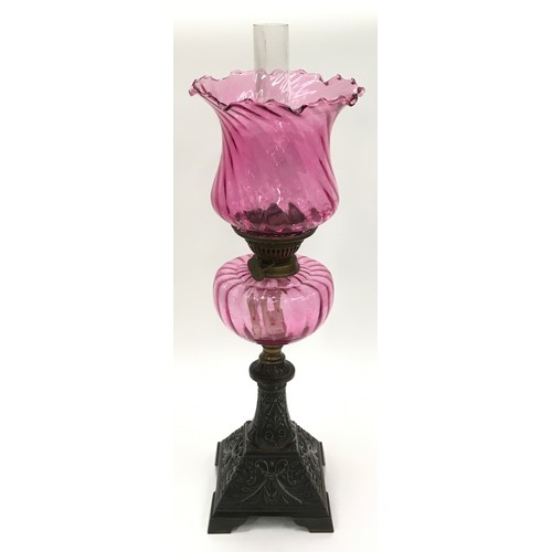 212 - Victorian cranberry glass oil lamp on cast iron base 64cm tall.