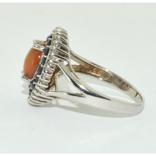 429 - Orange opal surrounded with blue/clear stones set in silver ring Size U