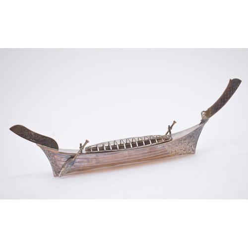 60 - A white metal long boat, with chased foliate decoration and mounted with two paddles/oars, stamped '... 