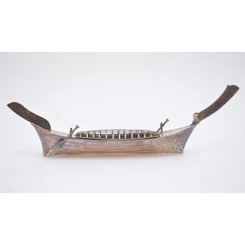 60 - A white metal long boat, with chased foliate decoration and mounted with two paddles/oars, stamped '... 